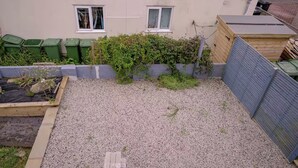 A residential backyard with a gravel surface, a wooden fence, and a green bush. - 1 Bedroom Apartment Sleeps 2 - Pets Welcome (St. Ives)