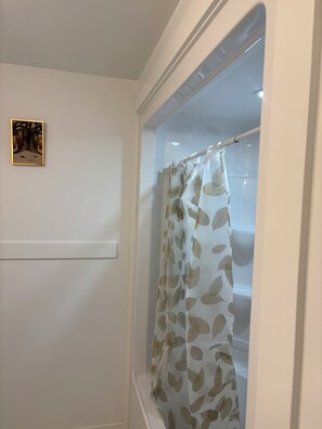 A bathroom with a shower curtain featuring a leaf pattern, a framed artwork on the wall, and a light switch. - The Pearl of Dieppe (Dieppe)