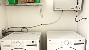 Two LG front-loading washing machines in a laundry room with a shelf above containing cleaning supplies. - The Pearl of Dieppe (Dieppe)