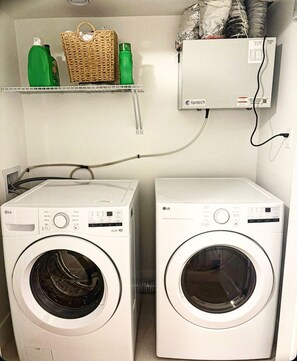Two LG front-loading washing machines in a laundry room with a shelf above containing cleaning supplies. - The Pearl of Dieppe (Dieppe)