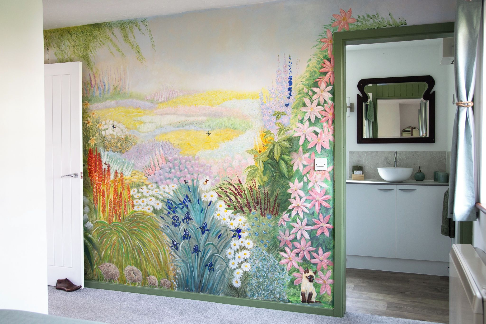 Une pièce avec un grand décor mural représentant des motifs floraux, une porte blanche et une salle de bain équipée d’un lavabo et d’un miroir.