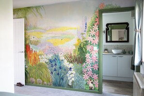 Ein Zimmer mit einer großen floralen Wandmalerei, einer weißen Tür und einem Badezimmer mit Waschbecken und Spiegel.