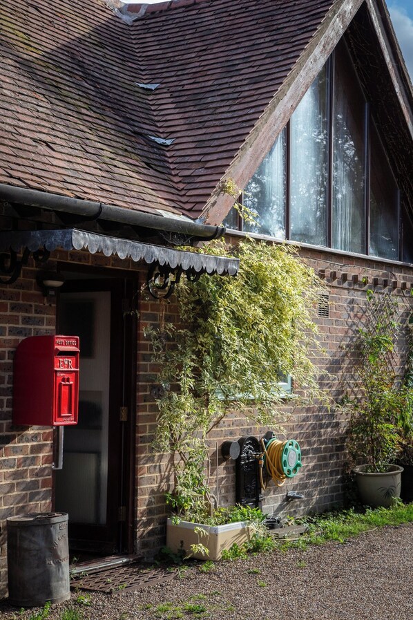 A brick building with a red post office mailbox, a green hose reel, and a potted plant.