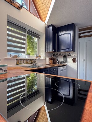 A compact kitchen with dark cabinetry, a window with blinds, and a built-in stove.