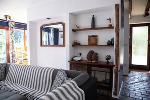 A living room with a sofa, a wooden console table with decorative items, a mirror, and a brick floor.