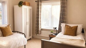 A bedroom with two single beds, a wardrobe, a radiator, and a window with curtains. - Three-bedroom house in Exmouth, sleeps 6 (Exmouth)