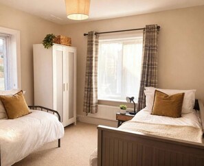 A bedroom with two single beds, a wardrobe, a radiator, and a window with curtains. - Three-bedroom house in Exmouth, sleeps 6 (Exmouth)