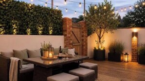 An outdoor patio with a dining table, wicker furniture, and string lights. - Three-bedroom house in Exmouth, sleeps 6 (Exmouth)
