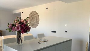 Uma área de jantar moderna com uma ilha central, cadeiras brancas e um vaso de flores.