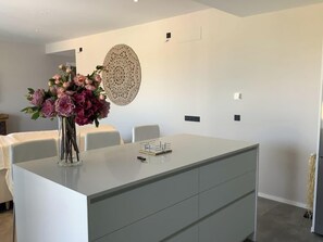 Ein moderner Essbereich mit einer zentralen Kochinsel, weißen Stühlen und einer Blumenvase.