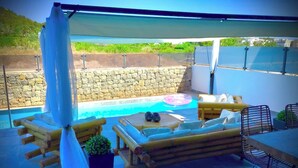 Uma área de estar coberta ao ar livre, com piscina, mobiliário de madeira e um painel de parede de pedra.