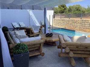 An outdoor seating area with a pool, stone wall, and a view of trees.