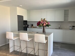 A modern kitchen with white cabinetry, a central island with bar stools, and a vase of flowers.