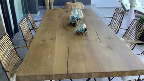 Uma mesa de jantar de madeira com cadeiras de vime, um banquinho trançado e castiçais de vidro.
