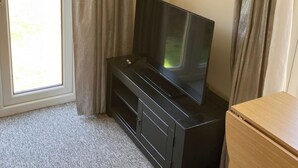 Una habitación con una televisión sobre un soporte negro, un mueble de madera y una ventana con cortinas.