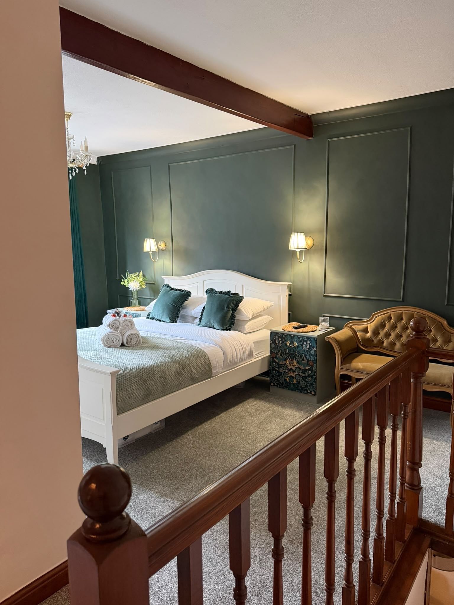 Une chambre à coucher avec un lit blanc, des murs verts, un escalier en bois et une table de chevet avec une lampe.