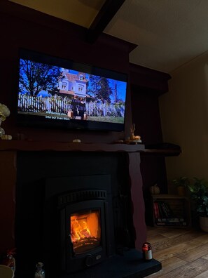 A television on a mantelpiece above a fireplace with a lit fire. - Cozy Cottage Retreat near Haworth, log burner (Keighley)