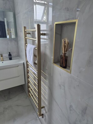 Une salle de bain avec un sol en marbre, un porte-serviettes, un meuble-lavabo avec un miroir et une petite étagère sur laquelle est posé un vase.
