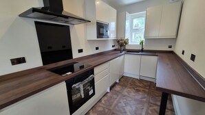A modern kitchen with white cabinets, a wooden countertop, a built-in oven, and a window providing natural light. - Apartment Sleeps 4 with Parking (Ilford)