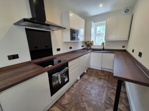 A modern kitchen with white cabinets, a wooden countertop, a built-in oven, and a window providing natural light. - Apartment Sleeps 4 with Parking (Ilford)