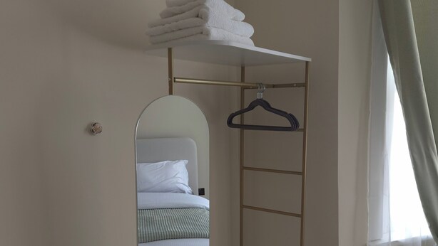 A compact room with a bed, a small walk-in closet with a mirror, and a window with sheer curtains. - Apartment Sleeps 4 with Parking (Ilford)