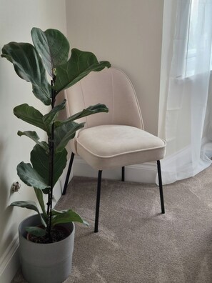 A corner of a room with a potted plant, a chair, and a carpeted floor. - Apartment Sleeps 4 with Parking (Ilford)