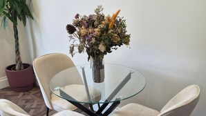 A dining area with a glass table surrounded by two chairs, a potted plant, and a vase with flowers. - Apartment Sleeps 4 with Parking (Ilford)