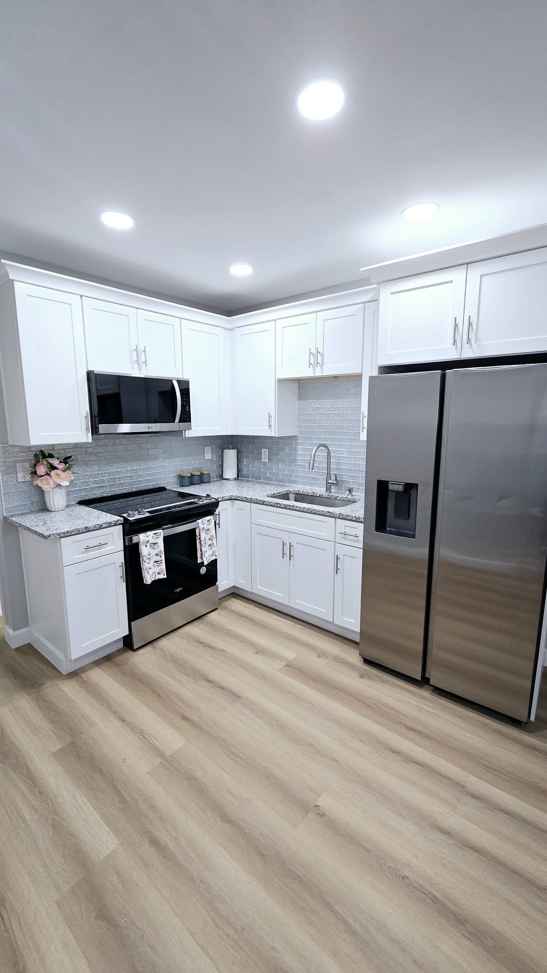 A modern kitchen with white cabinets, a stainless steel refrigerator, a microwave, and a gas stove.