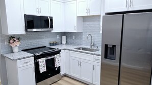 A modern kitchen with white cabinets, a stainless steel refrigerator, a microwave, and a gas stove. - Excellent 1-bedroom private studio (Gainesville)