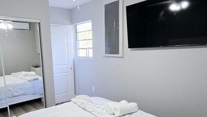 A bedroom with a bed, a ceiling fan, a TV, and a door. - Excellent 1-bedroom private studio (Gainesville)