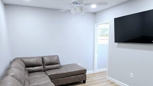 A modern living room with a sectional sofa, a ceiling fan, recessed lighting, and a flat-screen TV mounted on the wall. - Excellent 1-bedroom private studio (Gainesville)
