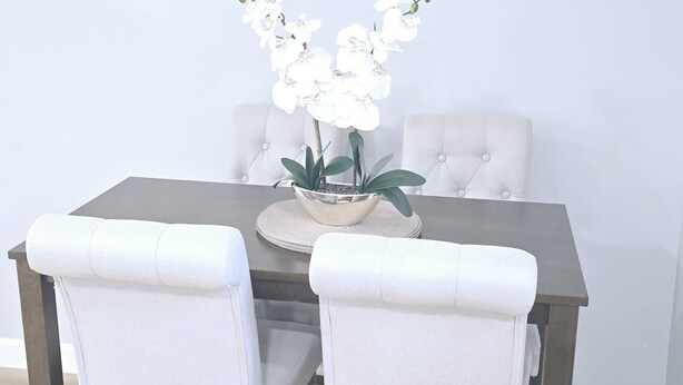 A dining area with a dark wooden table, white upholstered chairs, and a chandelier with multiple lights. - Excellent 1-bedroom private studio (Gainesville)
