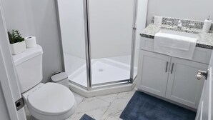 A modern bathroom with a glass shower enclosure, white marble flooring, and a sink with a granite countertop. - Excellent 1-bedroom private studio (Gainesville)