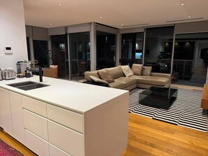 Un espai de vida modern amb una illa de cuina, un sofà i una àmplia porta de vidre que dona a un balcó.