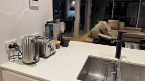 A modern kitchen with a built-in toaster, kettle, and coffee maker, a stainless steel sink, and a sliding glass door leading to a living area with a sofa and cushions. - 2B2B Executive Residence in Barton, 7-9 min walk to PH, M-Oval & Lake BG (Barton)