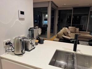 A modern kitchen with a built-in toaster, kettle, and coffee maker, a stainless steel sink, and a sliding glass door leading to a living area with a sofa and cushions. - 2B2B Executive Residence in Barton, 7-9 min walk to PH, M-Oval & Lake BG (Barton)