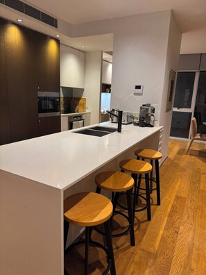A modern kitchen with a central island, wooden stools, and a coffee machine. - 2B2B Executive Residence in Barton, 7-9 min walk to PH, M-Oval & Lake BG (Barton)