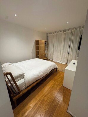 A bedroom with a wooden bed, a white bedside table, a wardrobe, and a curtain. - 2B2B Executive Residence in Barton, 7-9 min walk to PH, M-Oval & Lake BG (Barton)