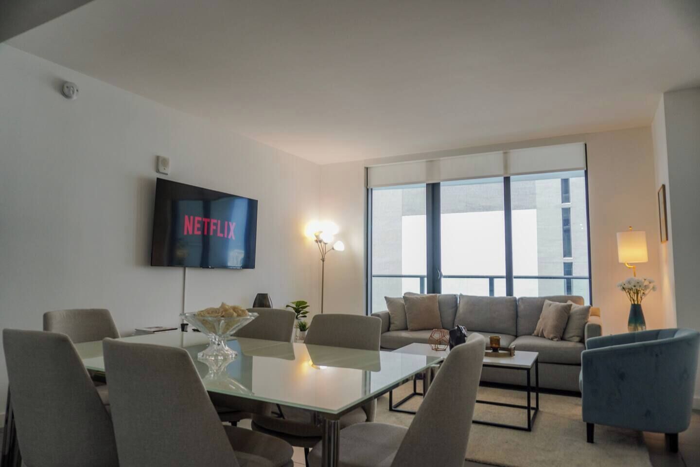 A modern living room with a glass coffee table, a sofa, and a TV mounted on the wall.