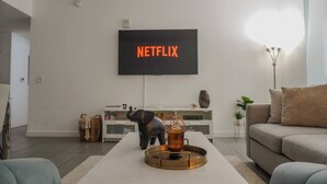 A modern living room with a flat-screen TV mounted on the wall displaying 'NETFLIX' in orange letters, a coffee table with a decorative object, and a sofa. - Luxurious 1BR condo in prime Location (Miami)