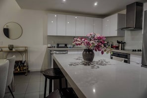 Eine moderne Küche mit weißen Schränken, einer zentralen Kochinsel mit Blumenvase und einem Essbereich mit Stuhl und kleinem Tisch.