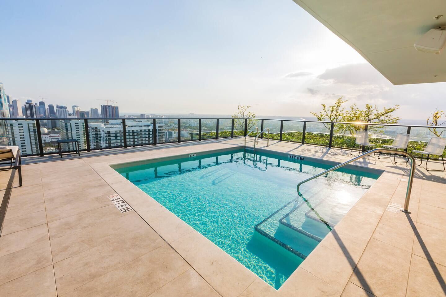 Una piscina en la azotea con vistas a la ciudad, barandilla de cristal y cielo despejado.