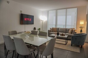 Een moderne woonkamer met een eethoek, een zithoek, een flatscreen televisie en een groot raam.
