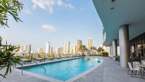 A rooftop pool with lounge chairs and a city skyline view. - Luxurious 1BR condo in prime Location (Miami)