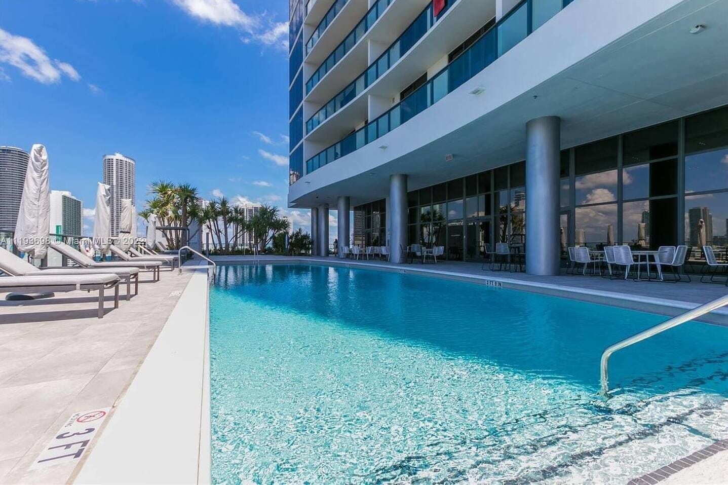 Una piscina en la azotea con sillones de descanso, un horizonte urbano de fondo y un edificio moderno con amplias ventanas.