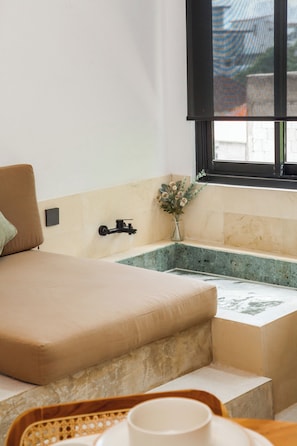 A room with a bed, a small window, a sink, and a vase with flowers.