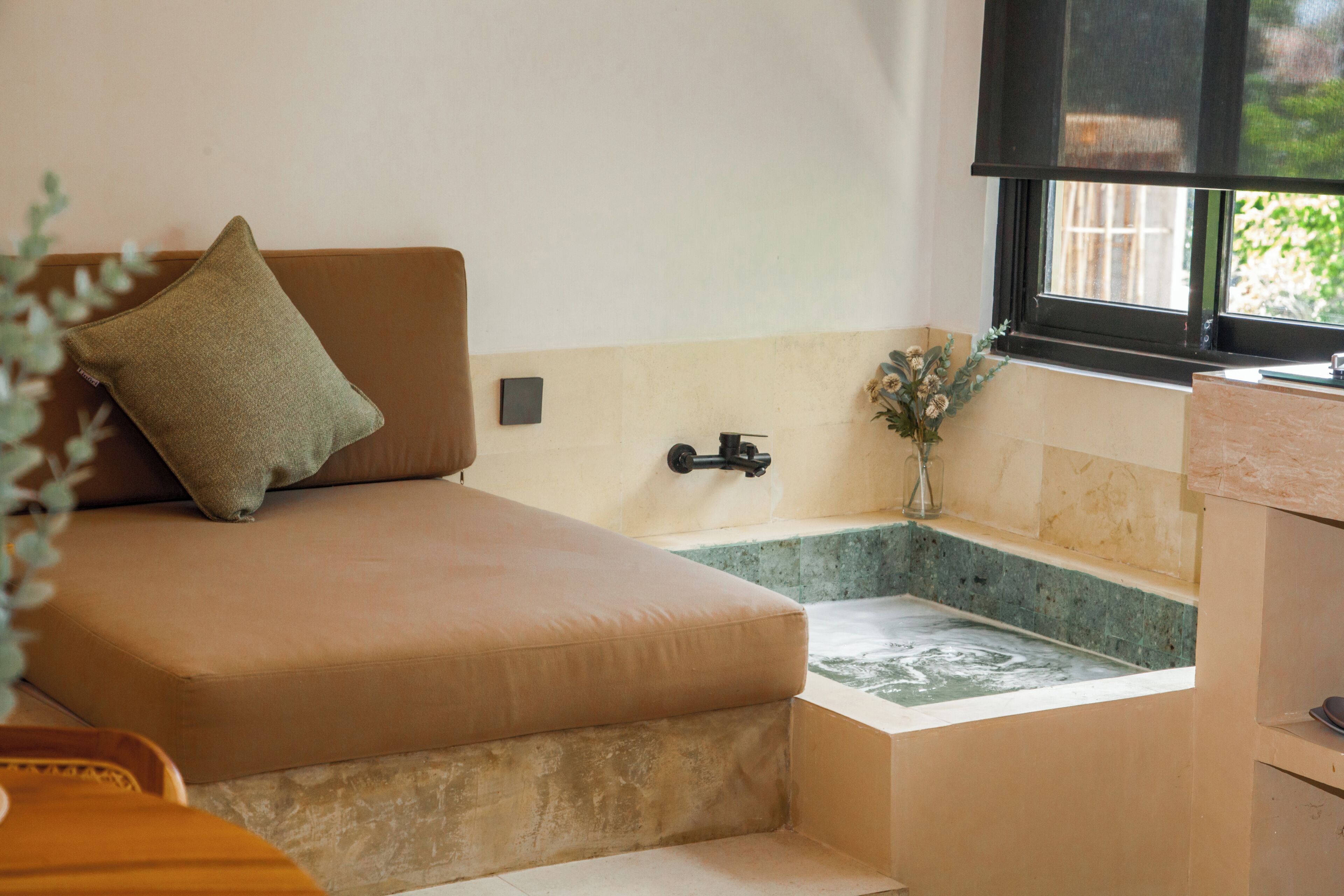 Ein kleiner, gemütlicher Raum mit Bett, Fenster, Waschbecken und einer kleinen Pflanze.