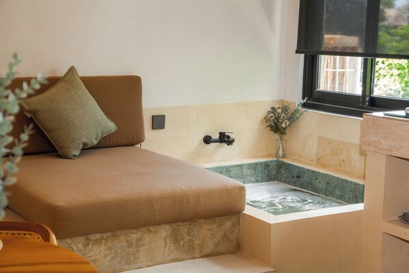 A small, cozy room with a bed, a window, a sink, and a small plant.