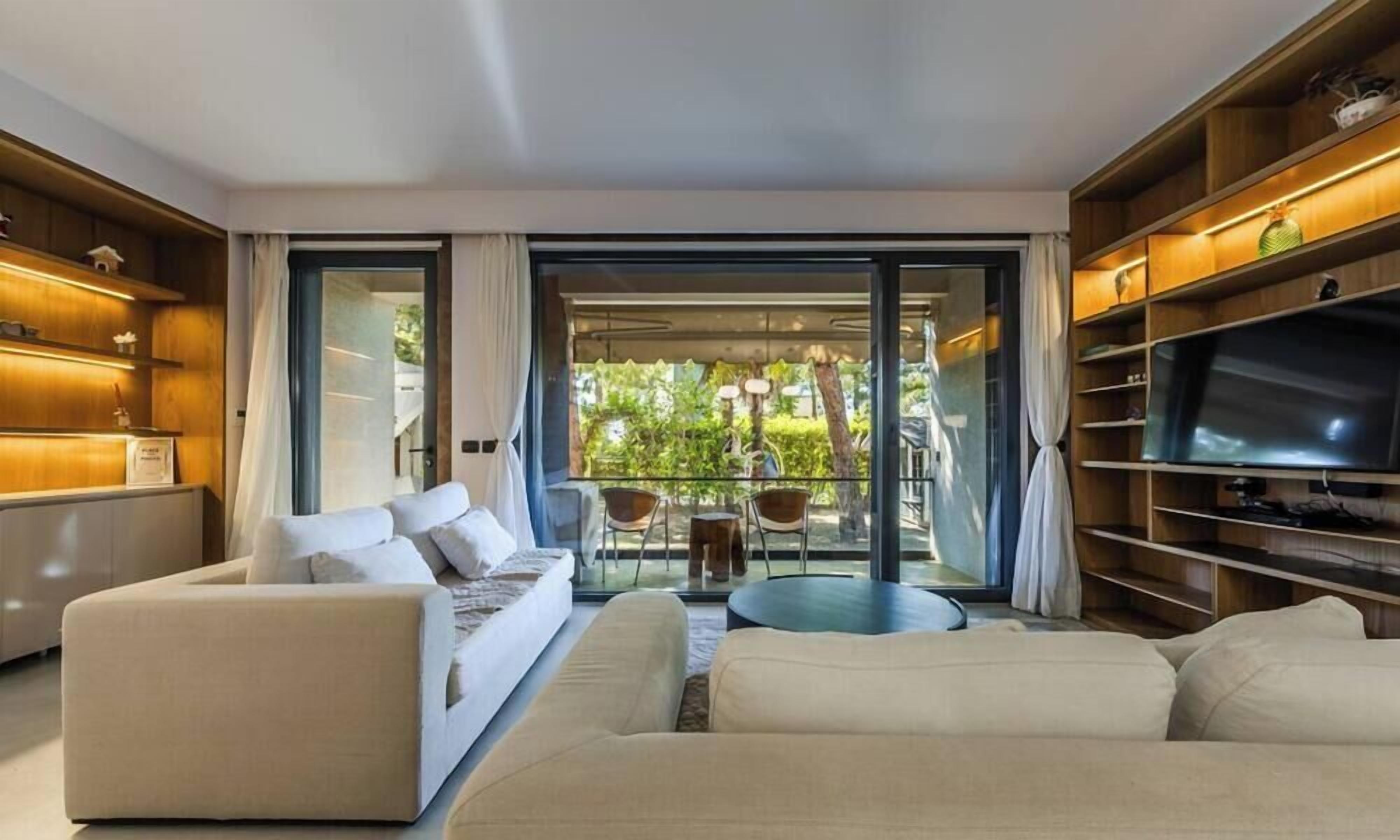 Una sala moderna con un sofá, televisor y un balcón con mobiliario exterior.