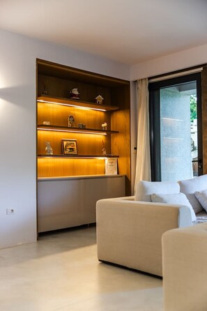 A modern living room with a built-in wooden shelving unit, a white sofa, and a large window with curtains. - Villa Flamingo 4BR Retreat in Valamar Residence (Sukth)